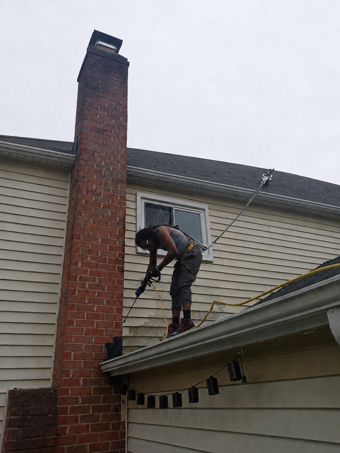 Royalty technician pressure washing a home while wearing fall-protection equipment